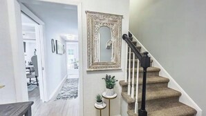 A staircase with a black handrail and beige carpeted steps, leading to a room with a white door and a small round table with a plant. - Beautiful 3 Bedroom Townhouse (Greensboro)