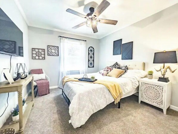 Une chambre à coucher avec un lit, des tables de chevet, un ventilateur de plafond et une fenêtre avec des rideaux.
