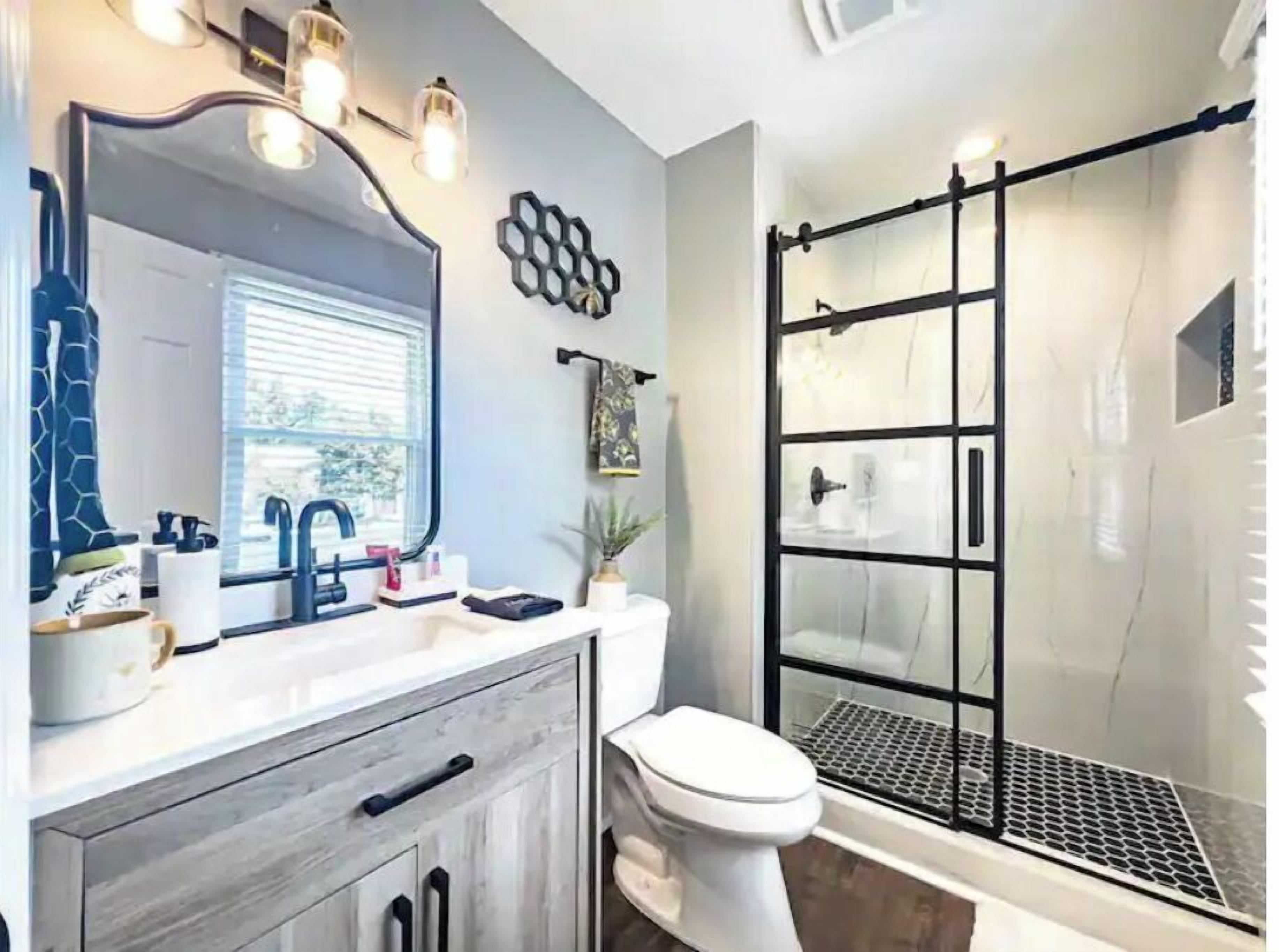 Un baño con diseño moderno, que incluye un espejo grande, un lavamanos, un inodoro y una cabina de ducha de vidrio.