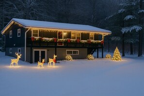 Una casa de dos pisos con un balcón, rodeada de nieve y decorada con luces y adornos navideños.