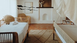 Une pièce chaleureuse avec un berceau en bois, une petite chaise, un lit et une étagère fixée au mur, sur laquelle est posé un vase de fleurs.