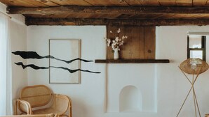 Une pièce avec un fauteuil en osier, un lampadaire à abat-jour en fibres tressées et une étagère murale ornée d’un vase de fleurs.