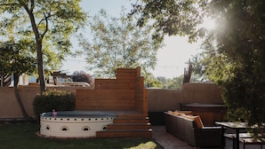 Un patio con jacuzzi, escalones de madera, mobiliario de mimbre y un sendero de ladrillos.
