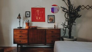 Una habitación con un aparador de madera, una lámpara, un cuadro enmarcado, una planta en maceta y un espejo montado en la pared.