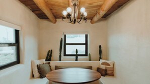A cozy seating area with a wooden table, a window with a view, and a chandelier. - Hot Tub + Pool! Cactus Suite at The Desert Compass (Albuquerque)