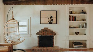 A cozy living room with a hanging chair, a fireplace, and a bookshelf. - Hot Tub + Pool! Cactus Suite at The Desert Compass (Albuquerque)