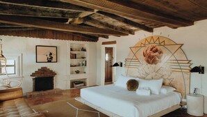 A bedroom with a large bed, a brick fireplace, a bookshelf, and a decorative wall mural. - Hot Tub + Pool! Cactus Suite at The Desert Compass (Albuquerque)