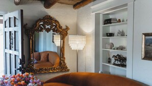 A room with a large ornate mirror, a brown leather sofa, a floor lamp, and a white shelving unit with various decorative items.