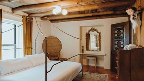 A room with a four-poster bed, a wicker chair, a mirror, and a wooden dresser.