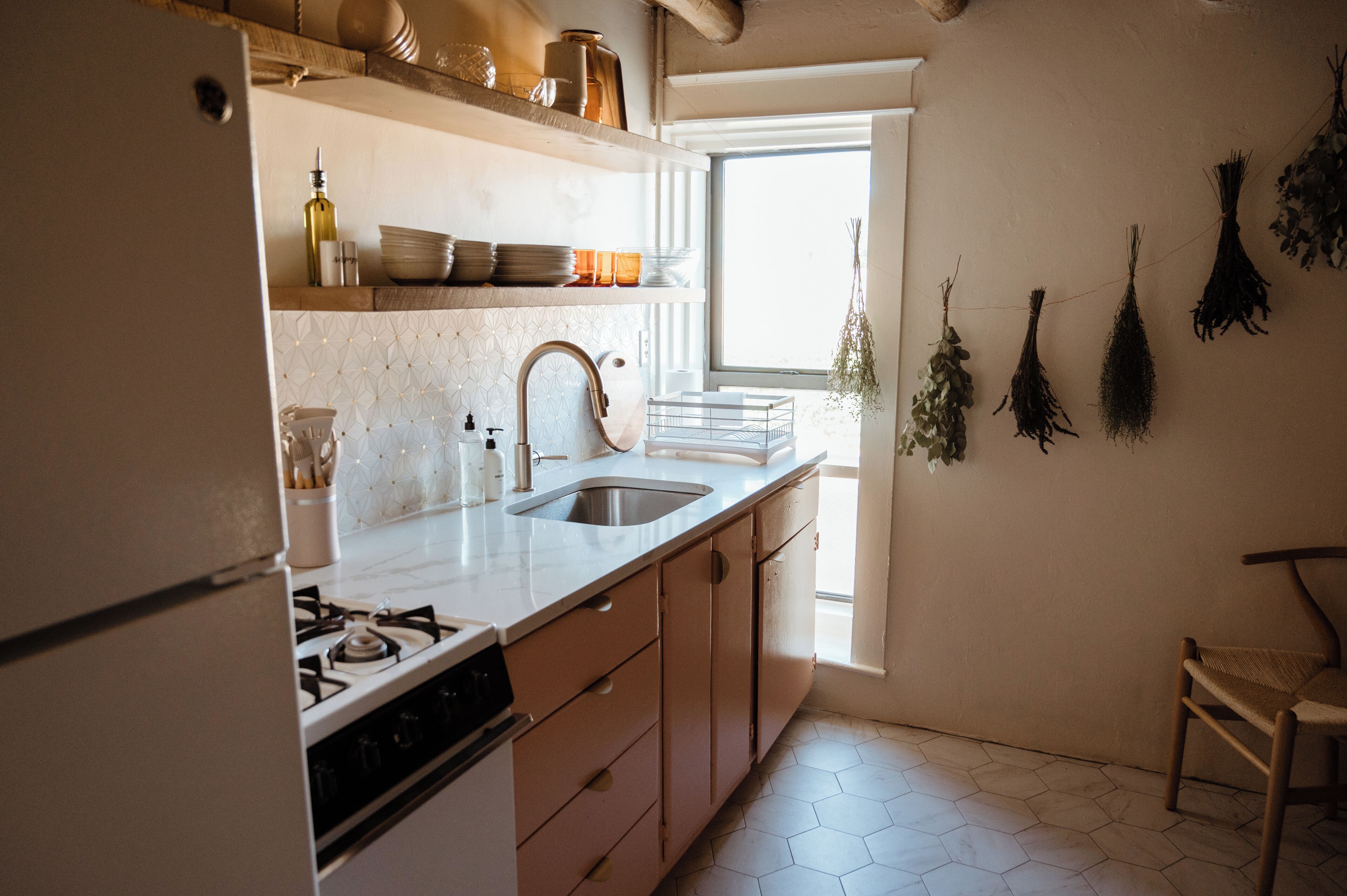 Una cocina con estufa a gas, pileta y armarios de madera. Hay repisas sobre la encimera con platos y una botella.