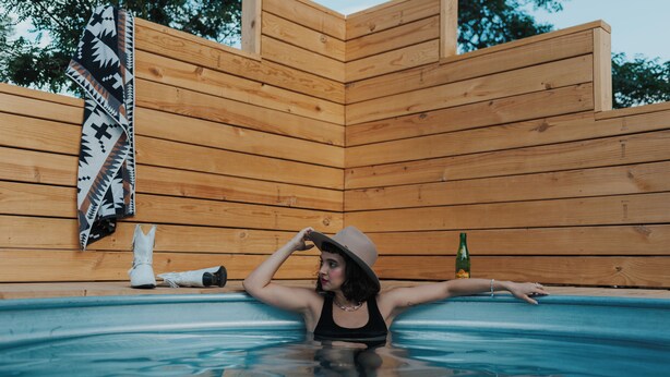 A person in a wooden cabin with a hot tub, a blanket, and a bottle.