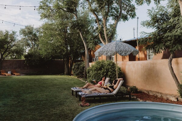 A backyard with a swimming pool, lounge chairs, and a patterned umbrella. - Hot Tub + Pool! Rattlesnake Suite at The Desert Compass in Old Town (Albuquerque)