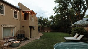 A backyard with a swimming pool, lounge chairs, a fire pit, and string lights. - Group Gatherings ☀ Property Buyout at The Desert Compass (Albuquerque)