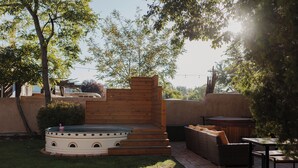 A patio area with a hot tub, wooden steps, wicker furniture, and a brick pathway. - Group Gatherings ☀ Property Buyout at The Desert Compass (Albuquerque)