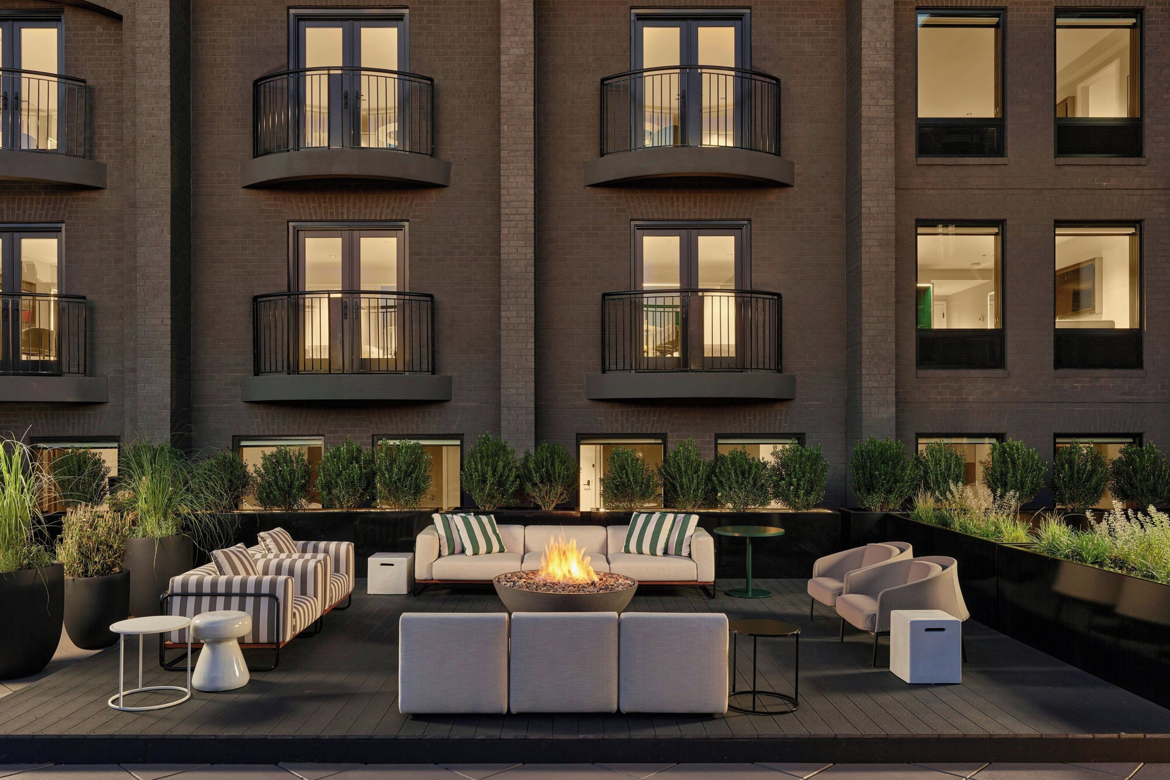 A modern outdoor seating area with a fire pit, sofas, and planters.