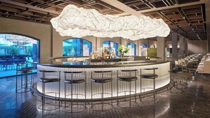 A modern bar area with a unique cloud-shaped light fixture, a bar counter, and multiple stools. - The Satire, Autograph Collection (Alexandria)