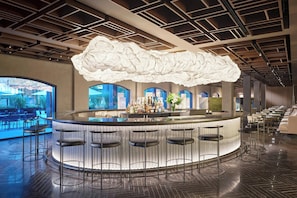 Un área de bar moderna con una lámpara de techo con forma de nube, una barra y varios taburetes.