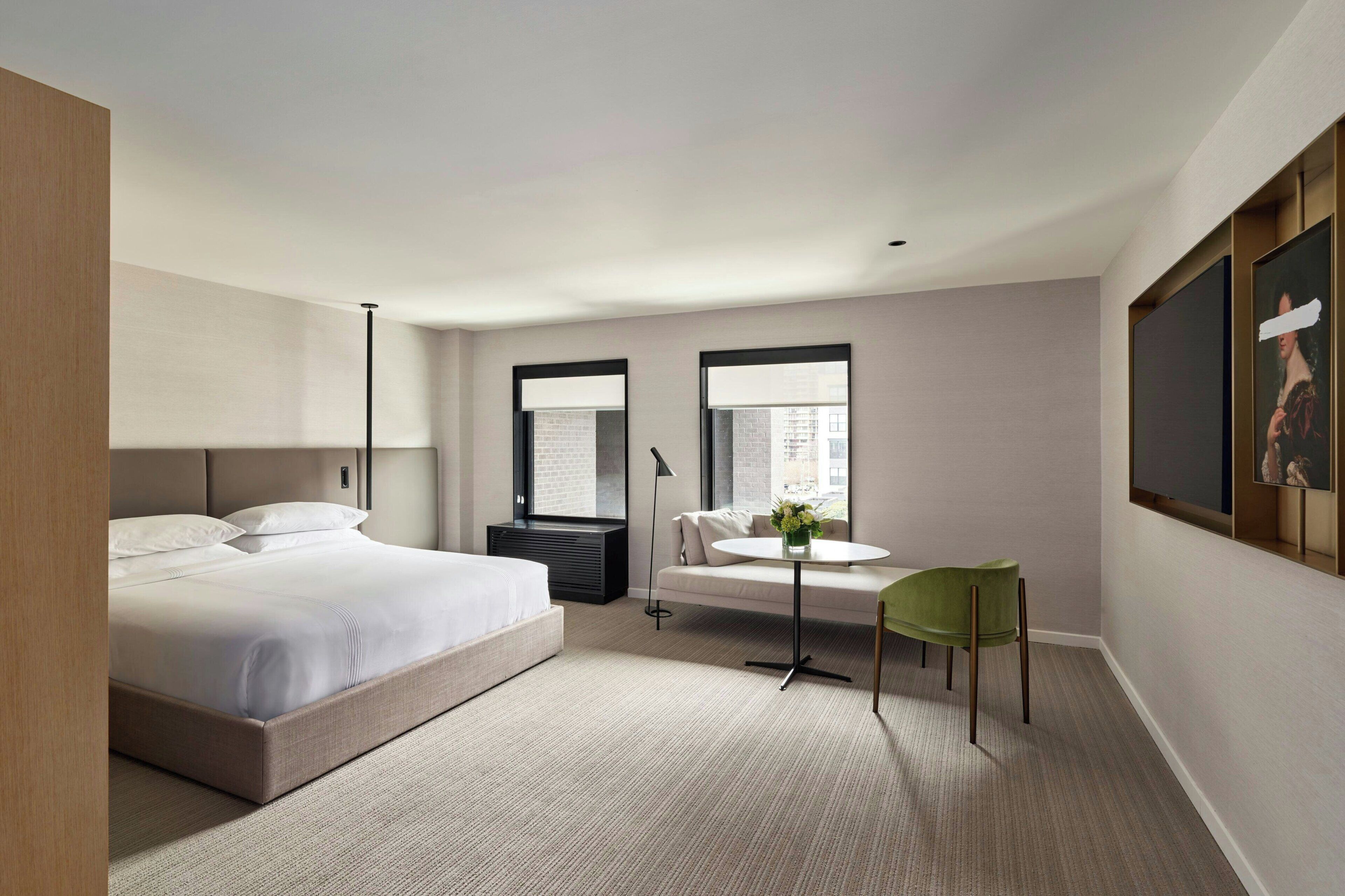 Ein modernes Hotelzimmer mit einem großen Bett, einem kleinen runden Tisch, einem grünen Sessel und einem großen Fenster.
