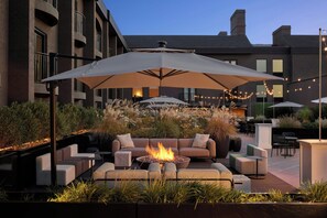 An outdoor seating area with a fire pit, sofas, and umbrellas.