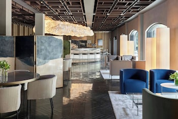 A modern hotel room with a long dining table, dark wood flooring, and large windows offering a view of the outdoors. at The Satire, Autograph Collection