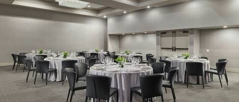 A conference room with round tables, black chairs, and a chandelier.