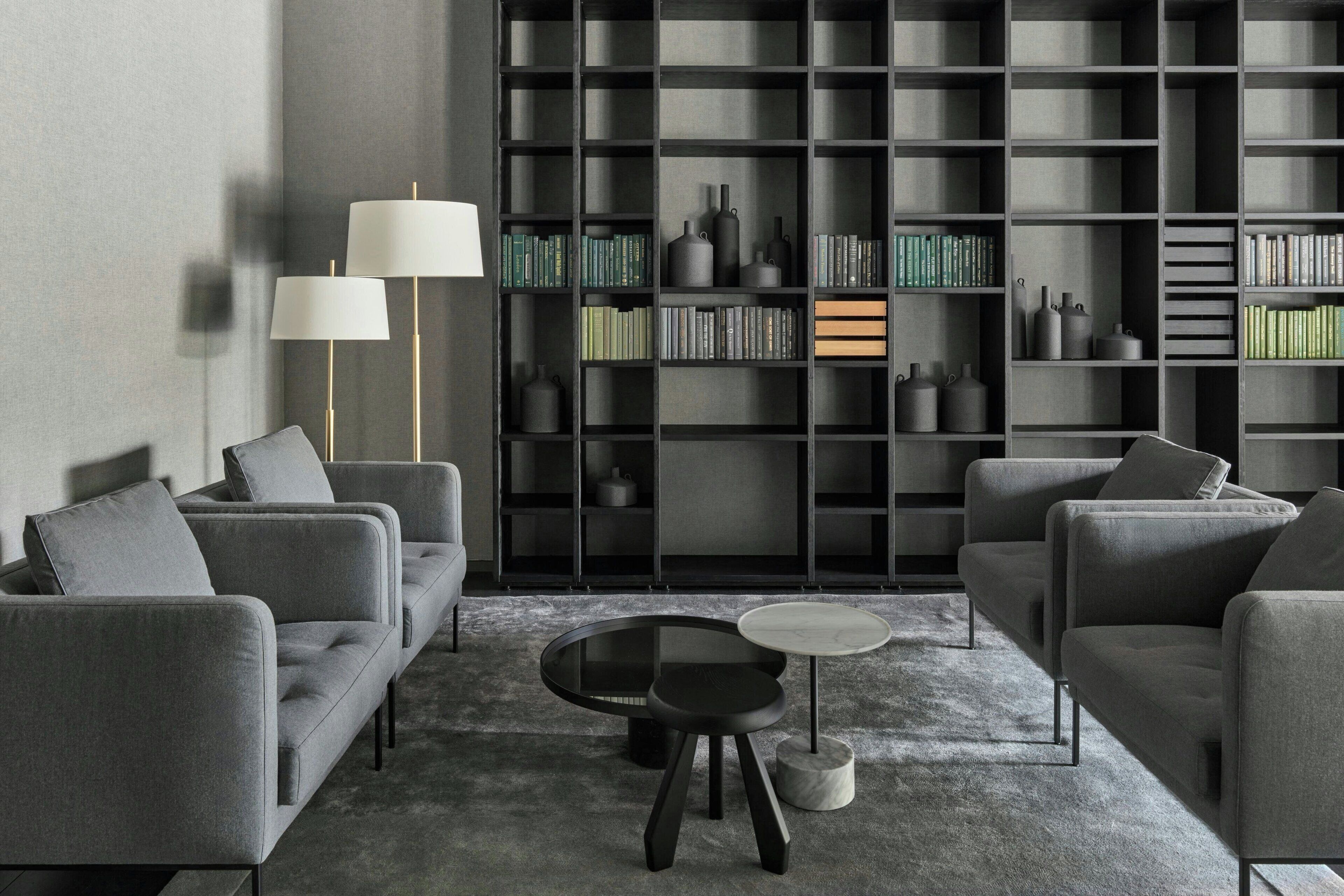 A modern living room with grey sofas, a glass coffee table, and a bookshelf filled with books and decorative items.