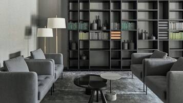 A modern living room with grey sofas, a glass coffee table, and a bookshelf filled with books and decorative items.