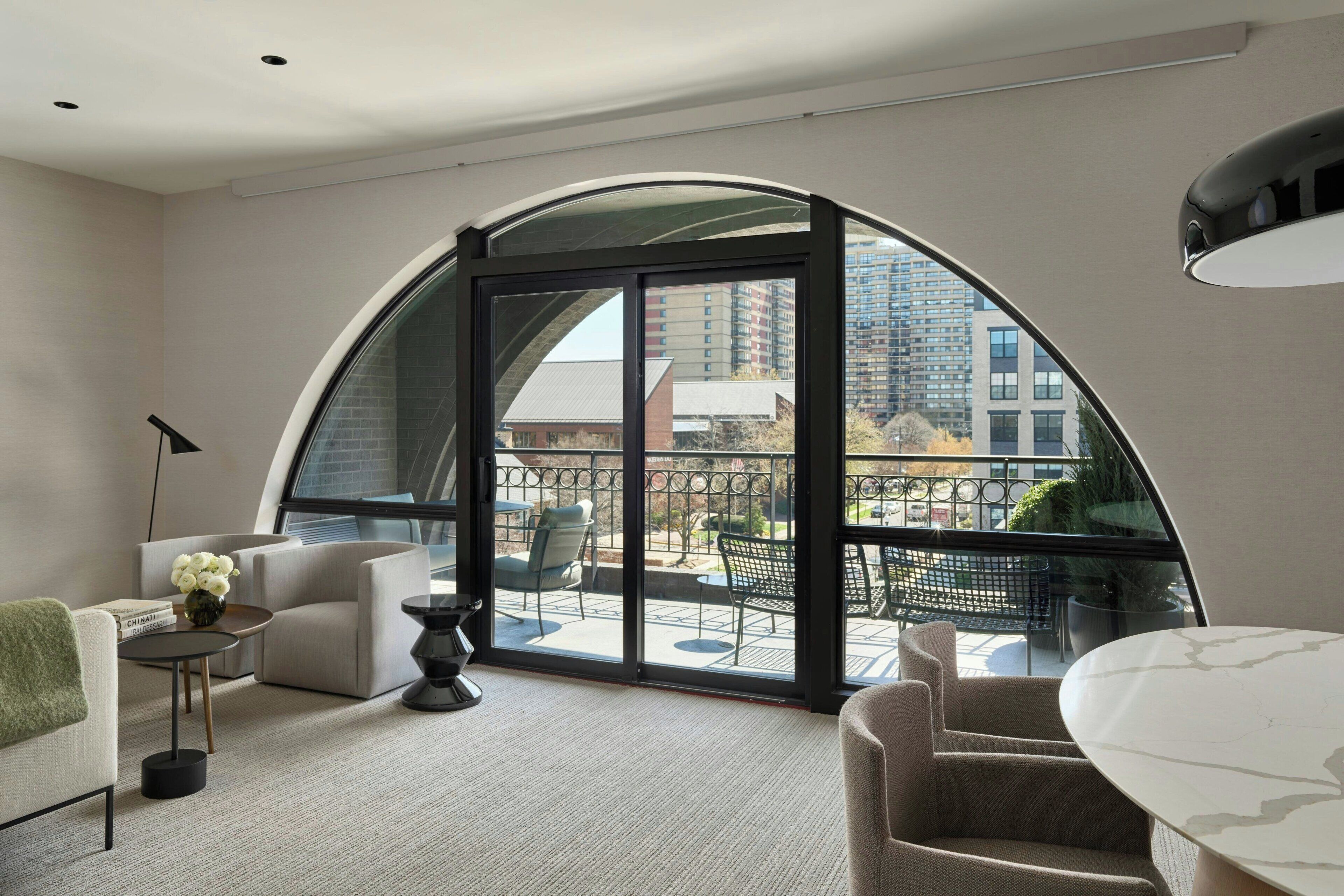 A modern living room with a curved glass wall, a sofa, a coffee table, and a dining table.