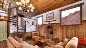Un intérieur rustique avec un escalier en colimaçon, des canapés en cuir, une cheminée et des murs en bois.