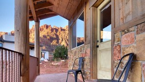 A wooden porch with two chairs, a stone wall, and a view of a mountain range. - Hideout @ the Rim - Jesse James Suite (Moab)