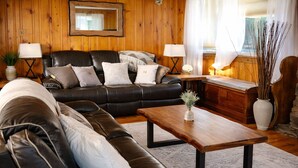 En stue med en sort lædersofa, et træbord og en hvid vase med grene.