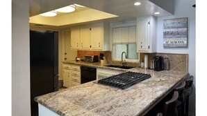 A kitchen with white cabinets, a granite countertop, a built-in stove, and a window with blinds.