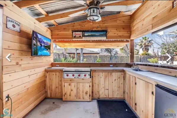 A wooden cabin with a kitchen area, a mounted TV, and a sign for 'Jameson'. - Bakersfield Outdoor Oasis - Kitchen, Bar, Pool, Spa, Fire (Bakersfield)