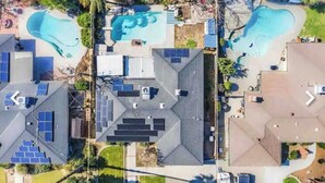 An aerial view of a residential area with multiple houses, solar panels, and two swimming pools.