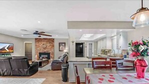A modern living room with a fireplace, a dining area with a table and chairs, and a kitchen in the background.
