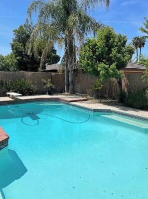 A swimming pool with a clear blue water, surrounded by a wooden fence and palm trees. - Bakersfield Outdoor Oasis - Kitchen, Bar, Pool, Spa, Fire (Bakersfield)