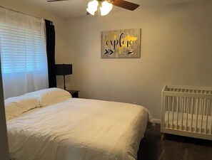 A bedroom with a bed, a crib, a ceiling fan, a wall-mounted lamp, and a motivational quote on the wall. - Bakersfield Outdoor Oasis - Kitchen, Bar, Pool, Spa, Fire (Bakersfield)