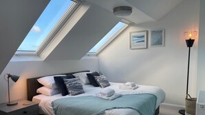 A bedroom with a skylight, a bed with pillows, a bedside table, a floor lamp, and two framed pictures on the wall. - Porth Oer, luxury accommodation (Nefyn)