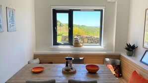 A dining area with a wooden table, two chairs, a bench, a window with a view of greenery, and a small table with a teapot and bowls. - Porth Oer, luxury accommodation (Nefyn)