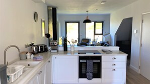 A modern kitchen with a central island, built-in appliances, and a view to a balcony. - Porth Oer, luxury accommodation (Nefyn)