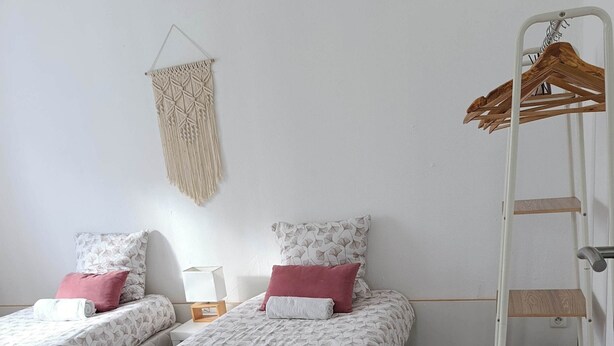 A bedroom with two single beds, a macrame wall hanging, a wooden hanger rack, and a wooden floor. - Detached house with enclosed garden (Abbeville)