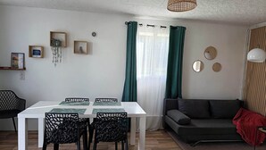 A modern living room with a dining area, featuring a white table, black chairs, a grey sofa, and a red throw blanket. - Detached house with enclosed garden (Abbeville)