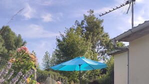A patio with a table and chairs, a blue umbrella, and a garden with flowers. - Detached house with enclosed garden (Abbeville)