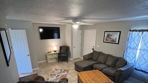 A living room with a sectional sofa, a coffee table, a chair, and a TV mounted on the wall. - Condo by Kataluma Nighlty Rentals! (Iowa Park)