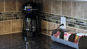 A kitchen with a black coffee maker, a tiled backsplash, and a coffee pod holder on the counter. - Condo by Kataluma Nighlty Rentals! (Iowa Park)