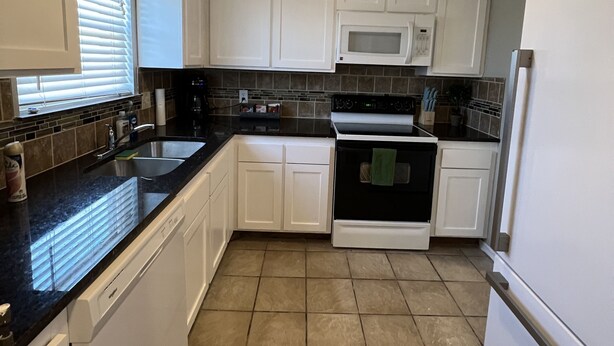 A kitchen with white cabinets, a black countertop, a microwave, an oven, and a refrigerator. - Condo by Kataluma Nighlty Rentals! (Iowa Park)