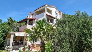A two-story building with a balcony, a covered patio, and a garden area with potted plants. - Apartments Jaklin - Two Bedroom Apartment with Terrace and Sea View (Rab)