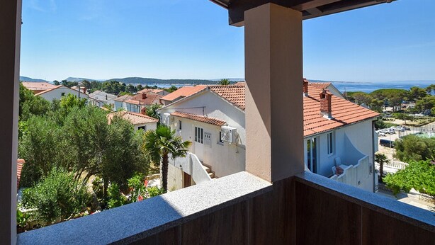 Un balcon offrant une vue sur une ville côtière, avec des maisons à étages et un ciel bleu dégagé.