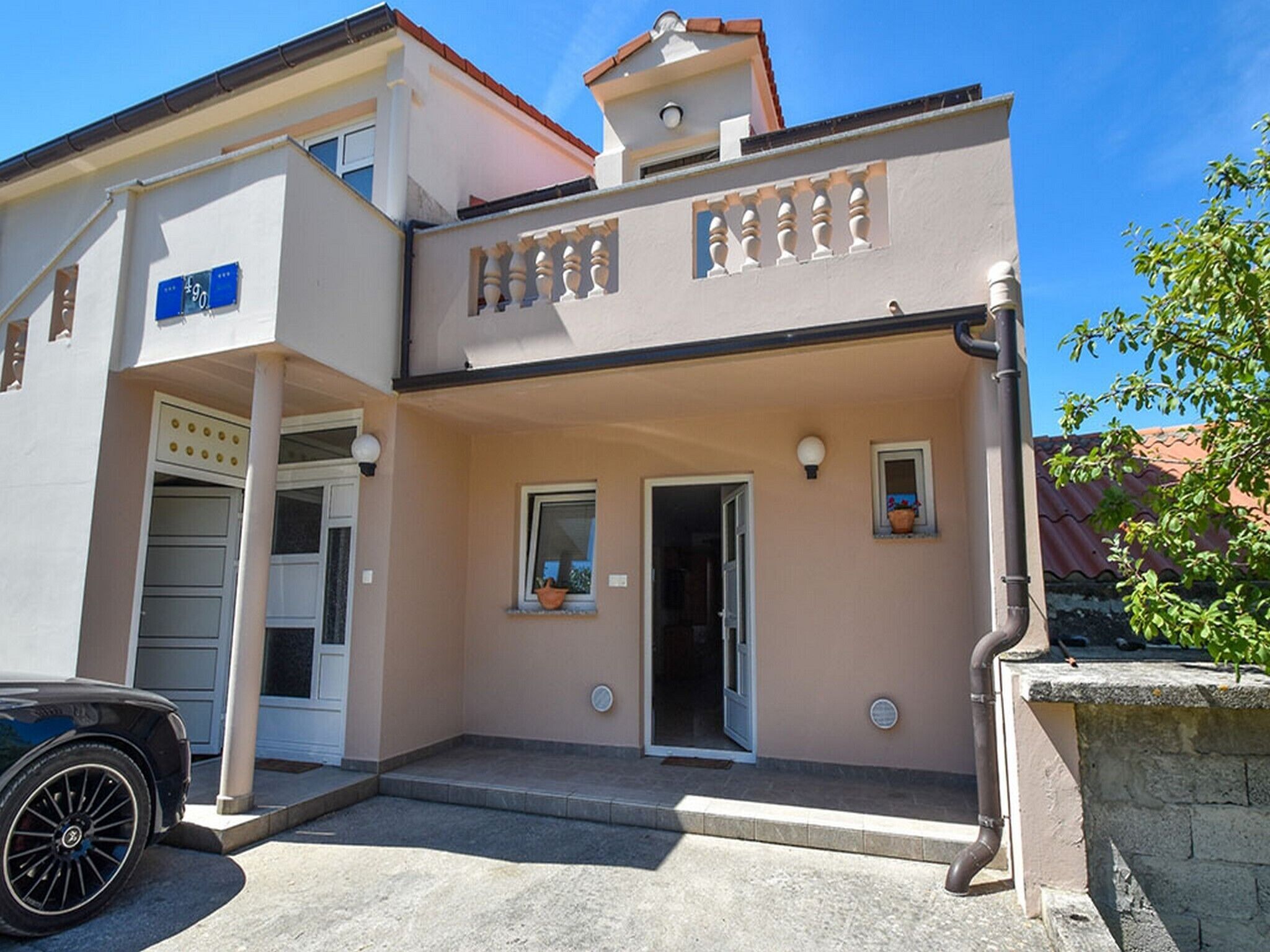 A two-story building with a beige facade, a covered entrance, and a small balcony with decorative railings.
