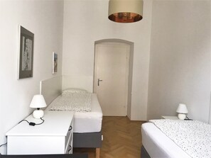 Een kleine, schone kamer met twee bedden, een bureau en een deur naar een andere kamer.